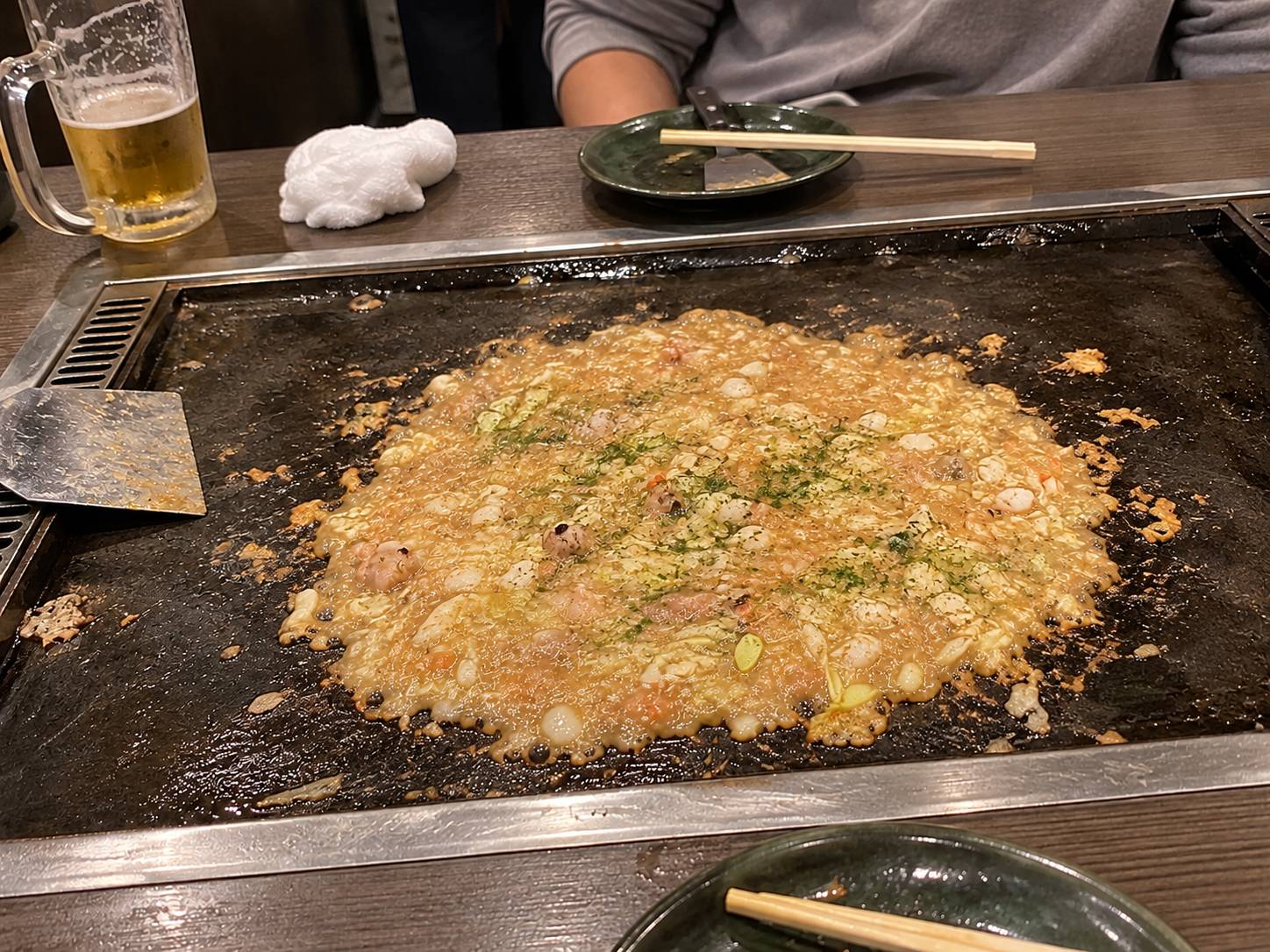 A thin, bubbling layer of monjayaki with cabbage and toppings, sprinkled with green aonori seaweed
