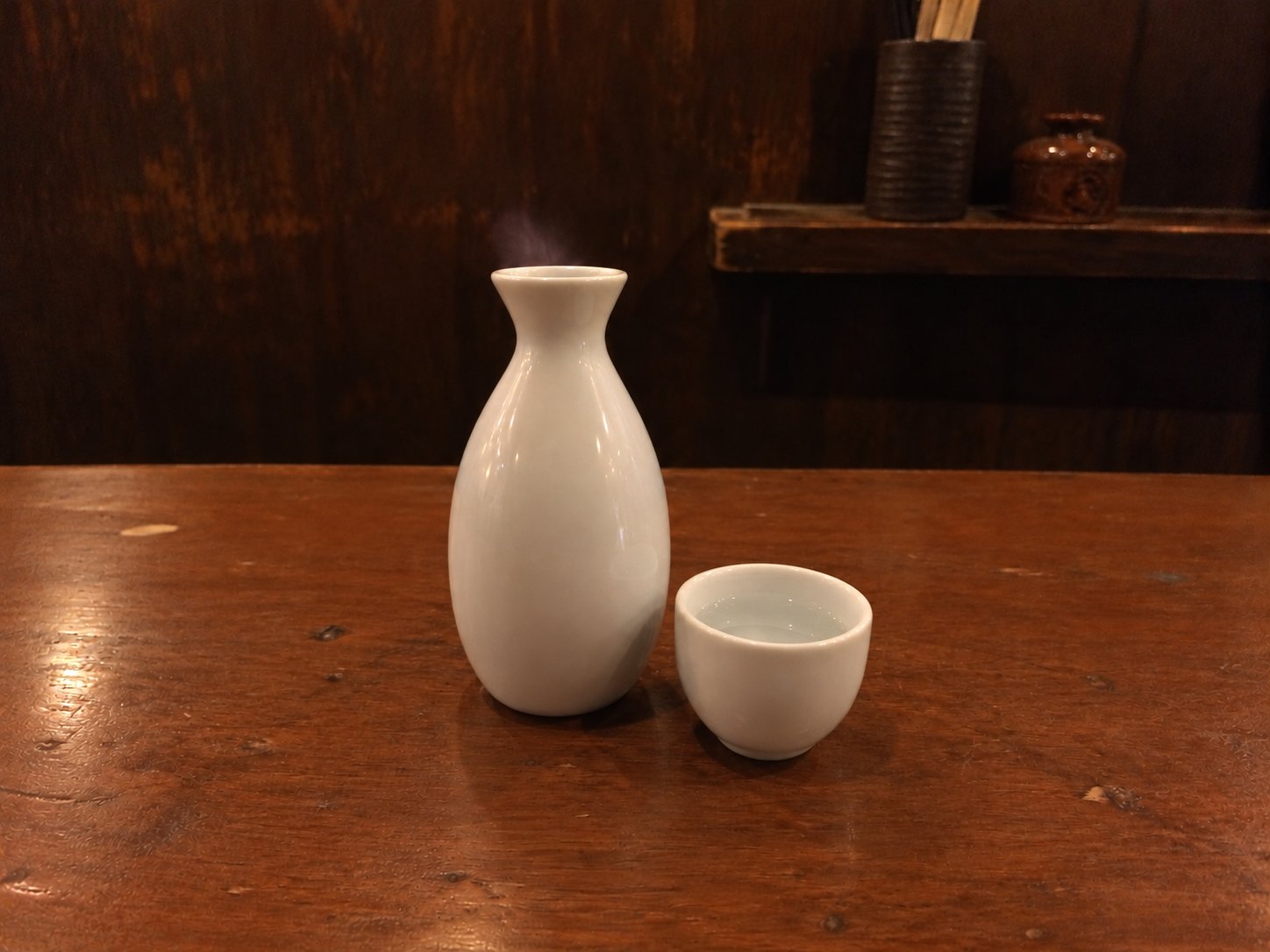 A white sake flask with a little steam rising from it, next to a small cup