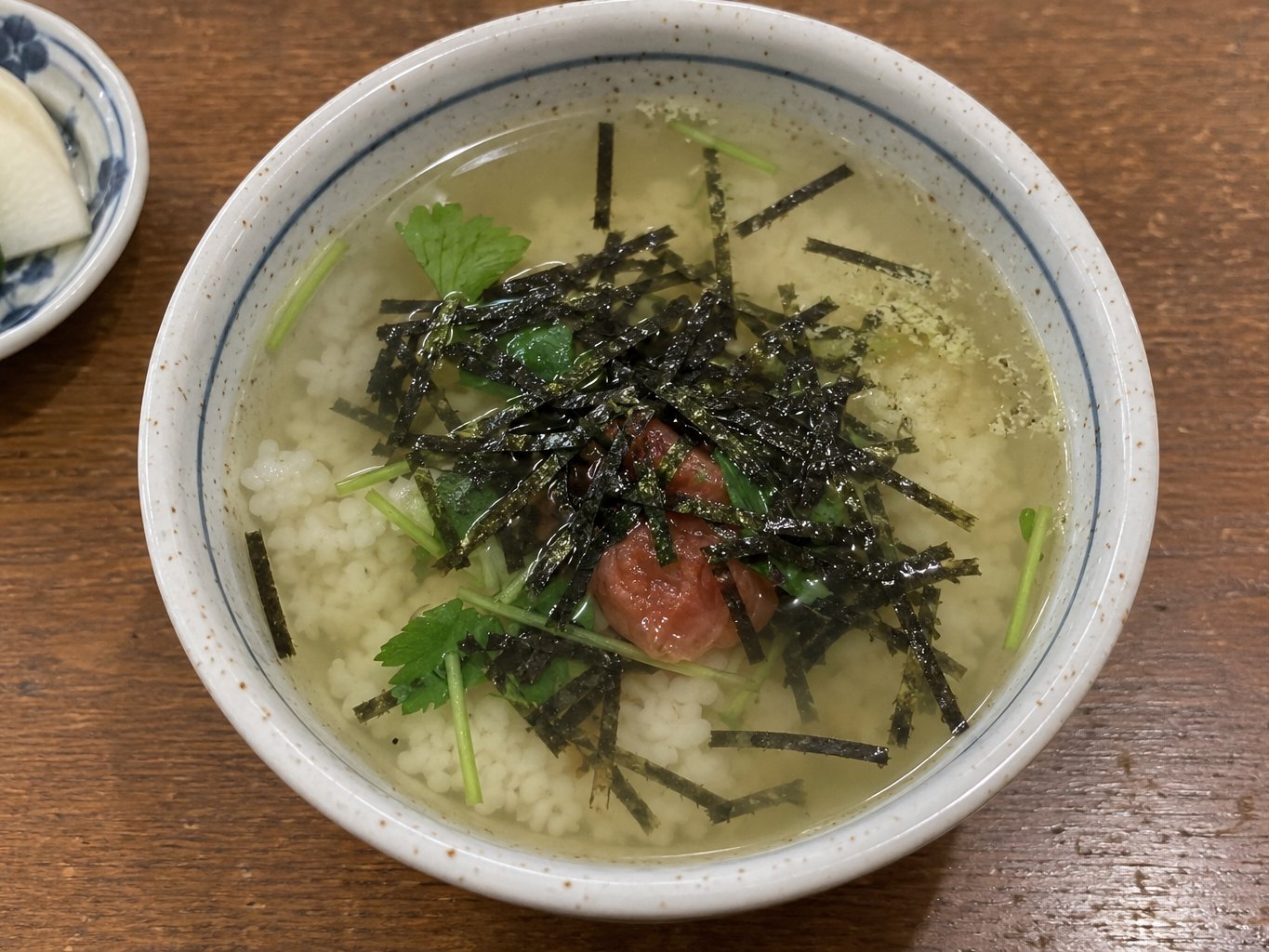 A bowl of ochazuke: rice with a pickled plum, nori and green tea poured over, on an izakaya counter