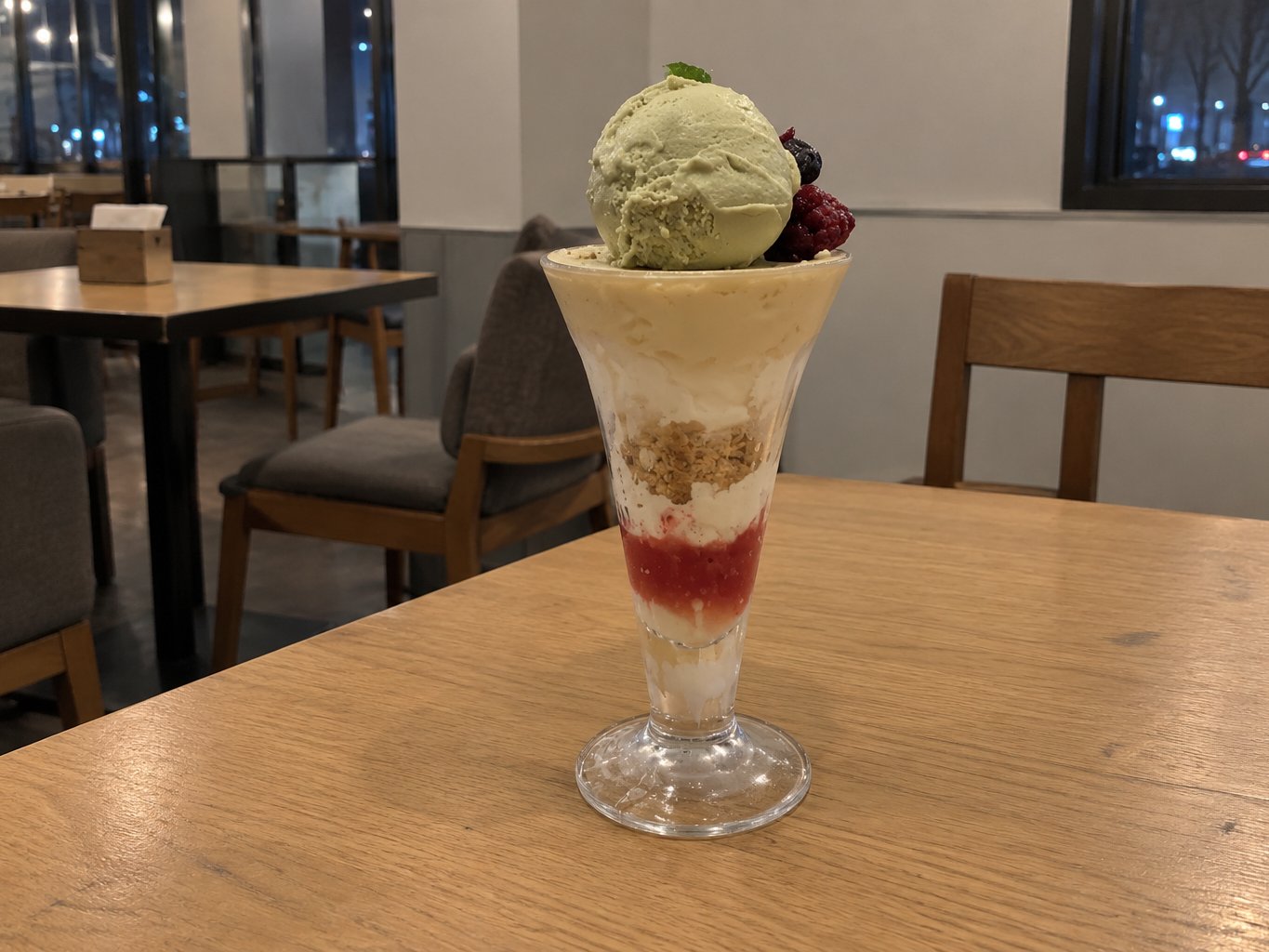 A tall parfait with ice cream, fruit and layers in a glass, served at night