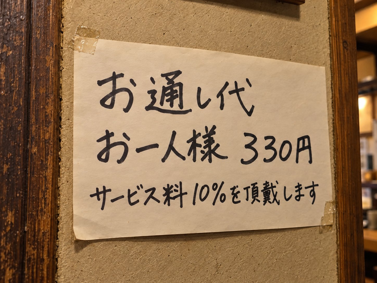 A handwritten sign at an izakaya: otoshi 330 yen per person, and a 10% service charge